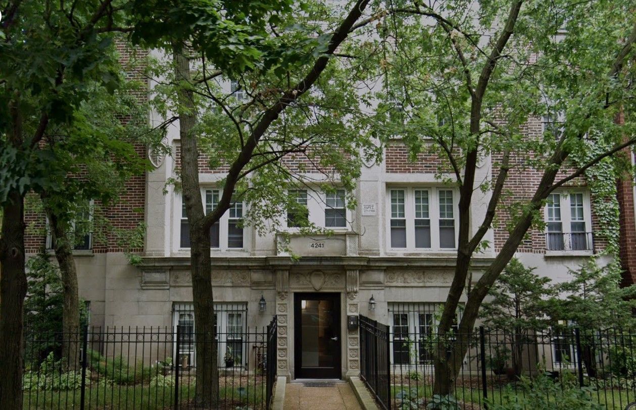 A large brick building with a fence around it and trees in front of it.