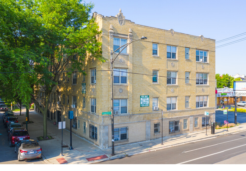 An aerial view of a large apartment building with cars parked in front of it.