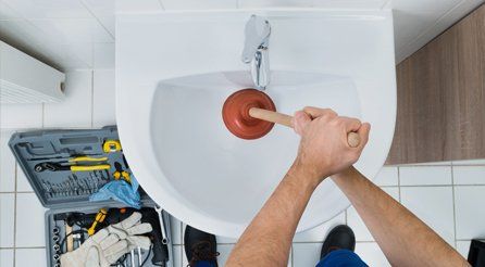 A plumber using a plunger on a bathroom sink