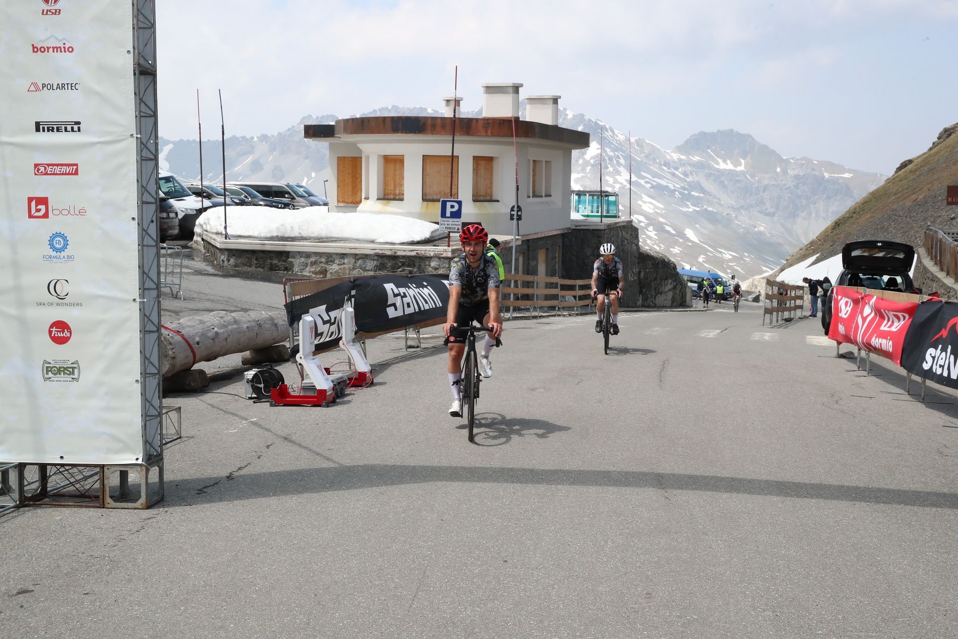 A man is riding a bike down a road next to a sign that says ' bosch ' on it