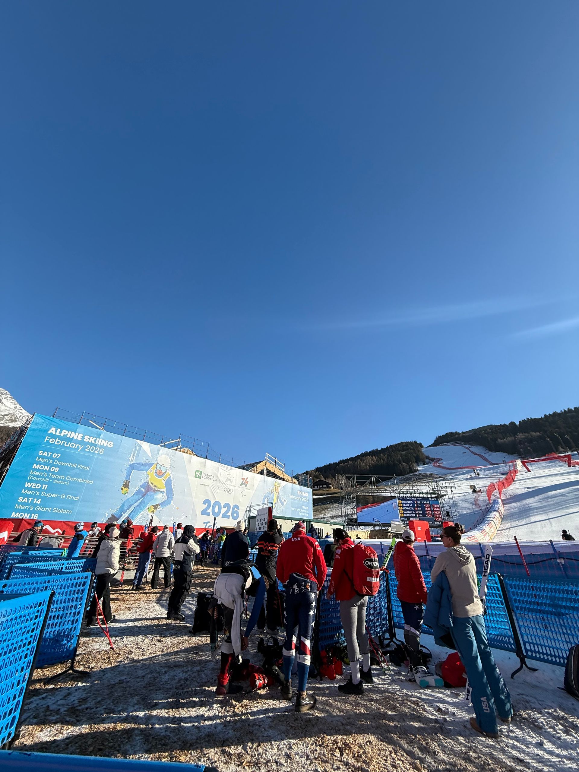 A group of people are standing in the snow near a sign that says Bormio 2026