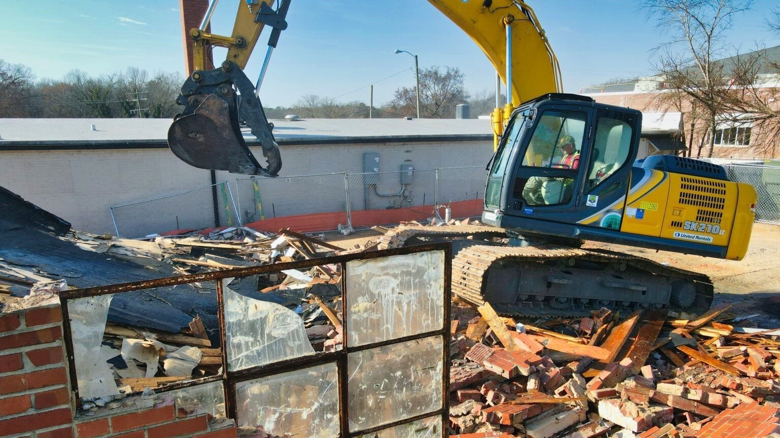 A yellow and blue excavator is demolishing a building.