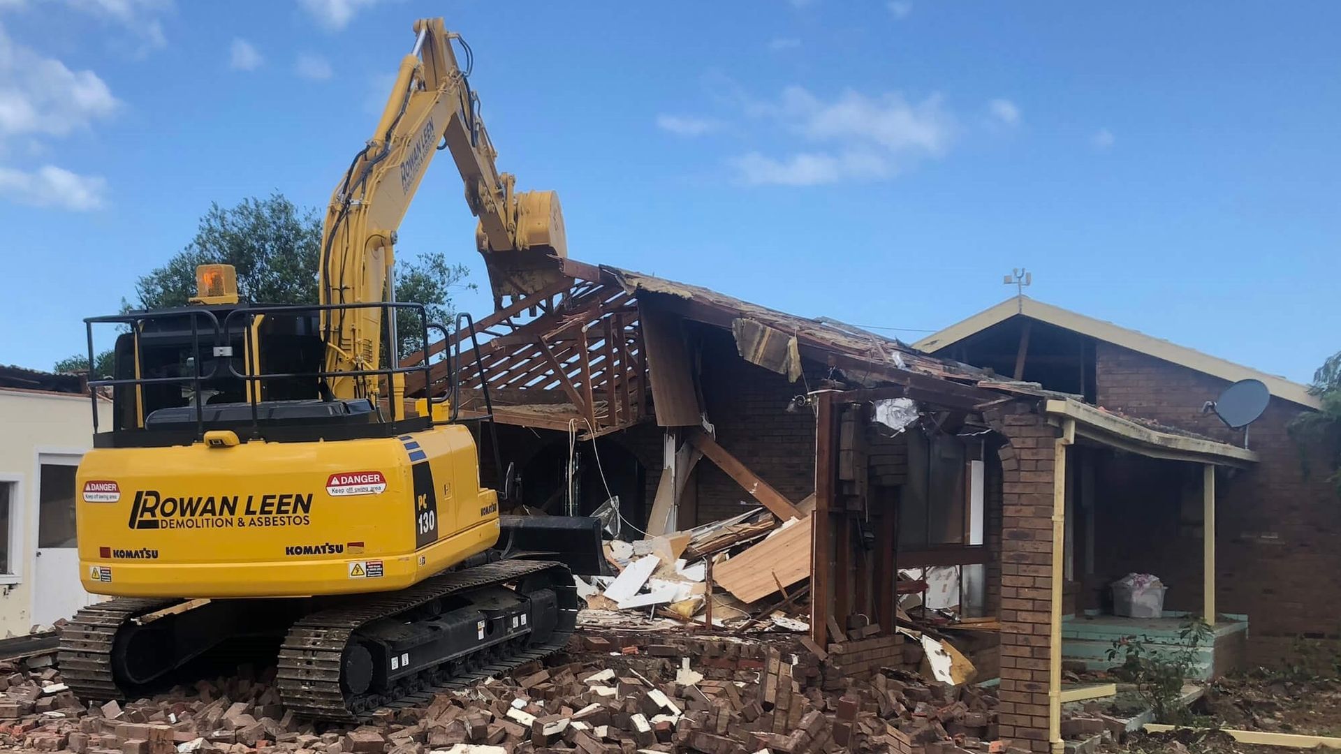 A large yellow excavator is demolishing a house.