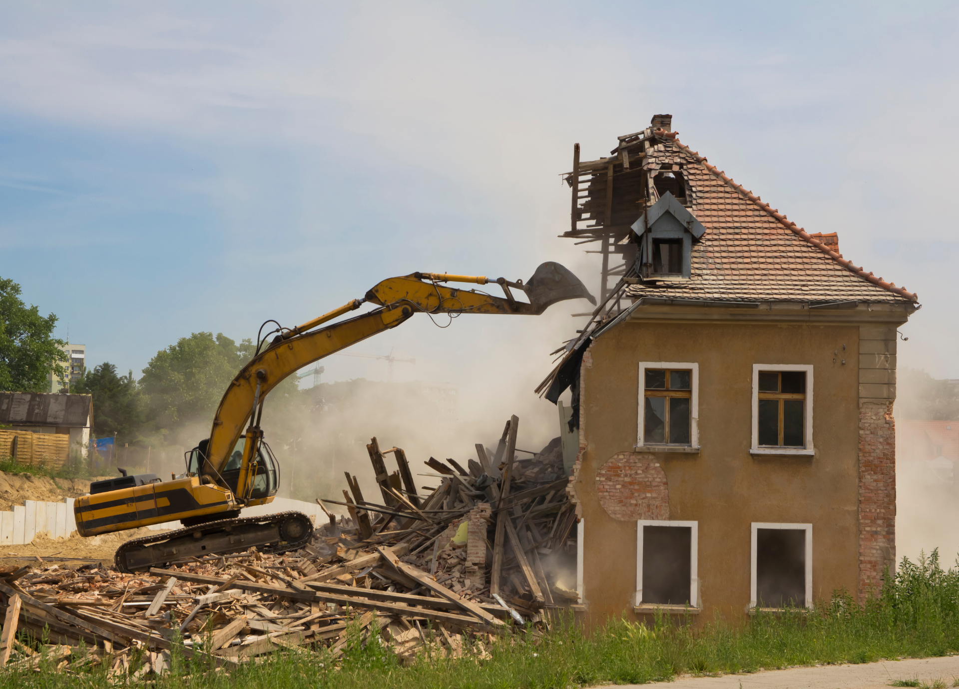 A large yellow excavator is demolishing a house.