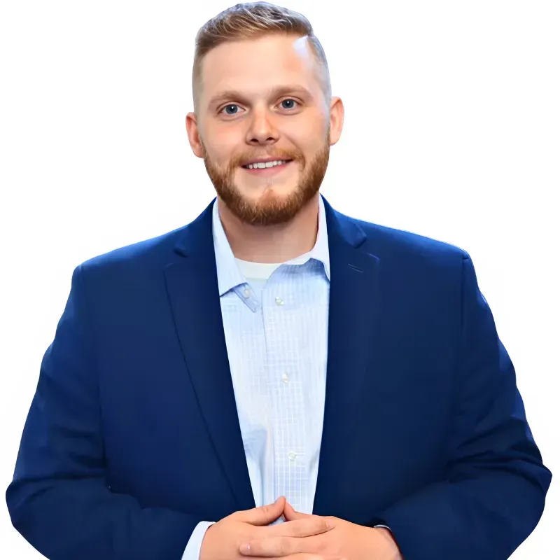 Man in a blue blazer and light blue shirt smiles, hands clasped. White background.
