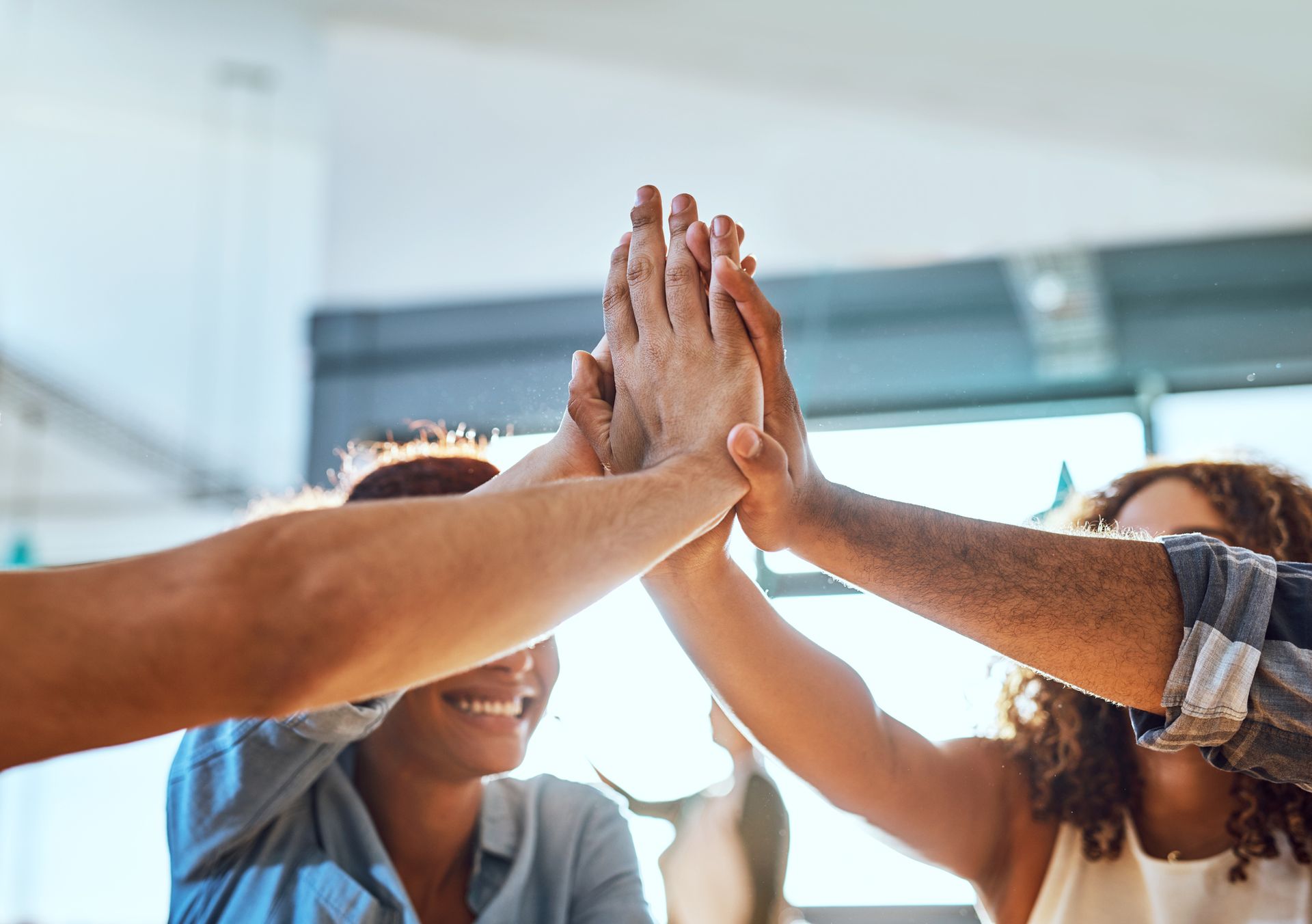 Hands in a high-five, celebrating. People smiling in a brightly lit office setting.
