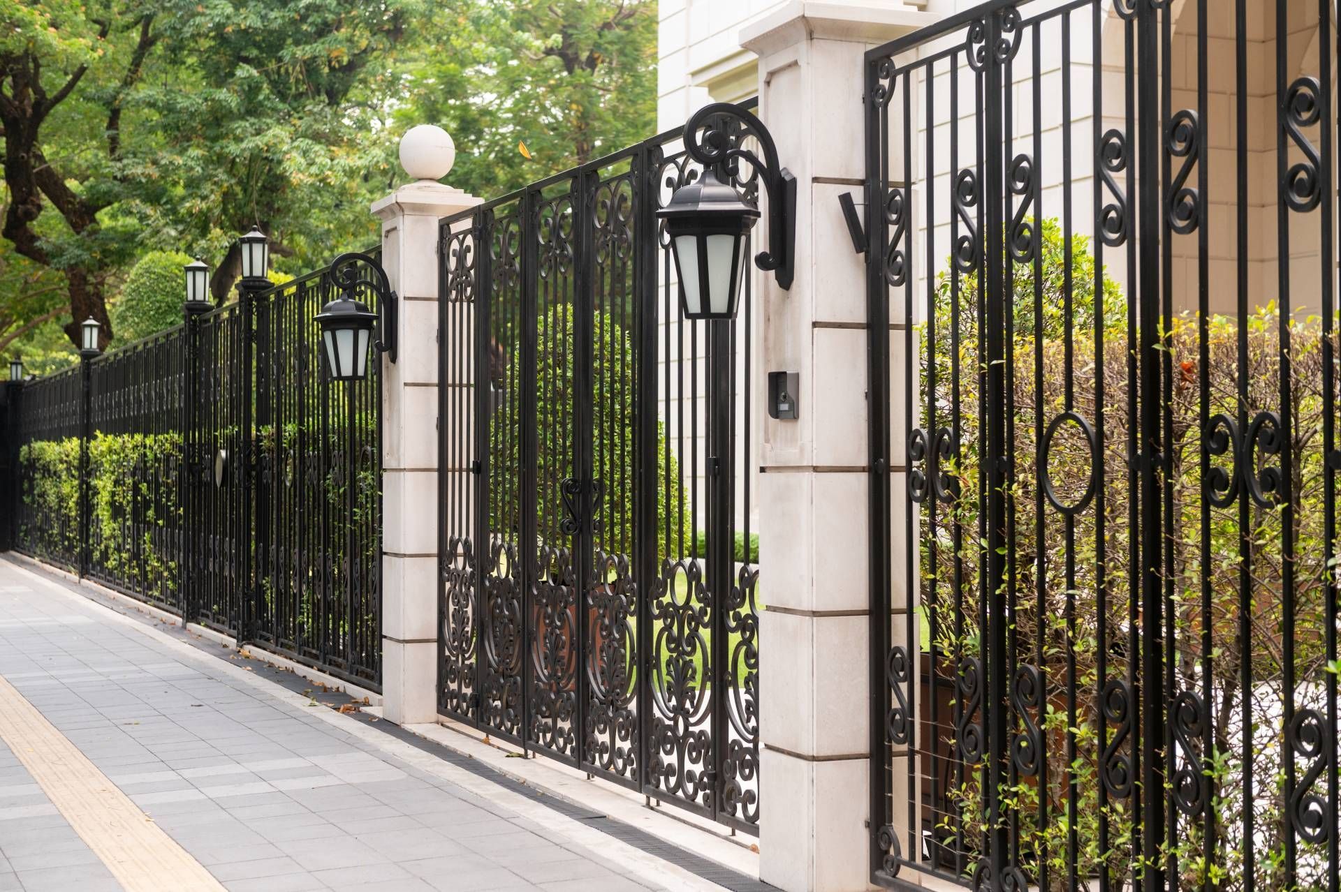 Black wrought-iron fence with white pillars along a tree-lined sidewalk