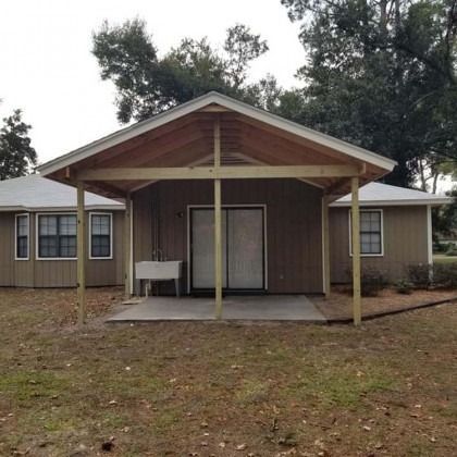 Single-story house with a covered front porch and sliding glass door, set on a grassy yard.