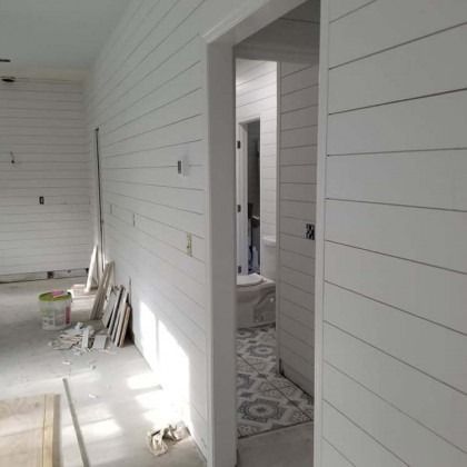 White interior hallway and unfinished room with stacked boards, tools, and open doorway to a tiled bathroom.
