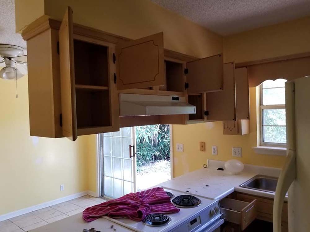 Open kitchen with light wood cabinets, beige walls, white counters, and a windowed sink area.