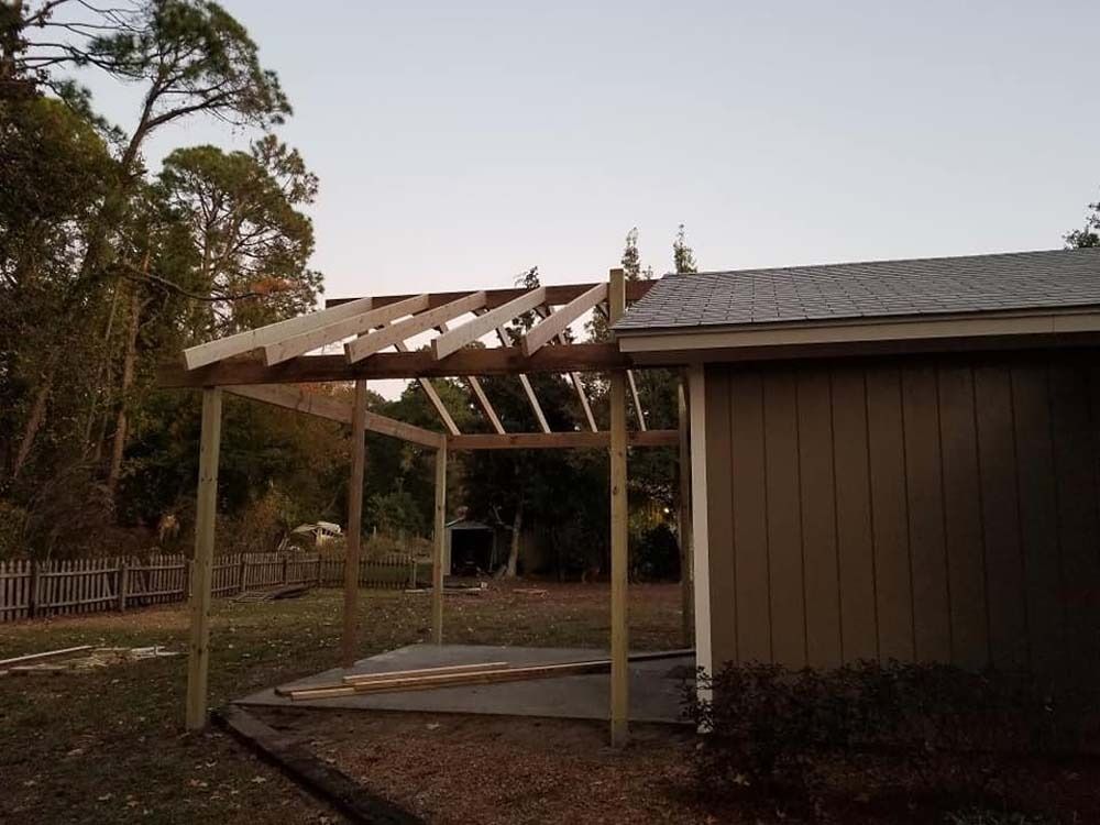 Partially built wooden pergola beside a brown house in a yard