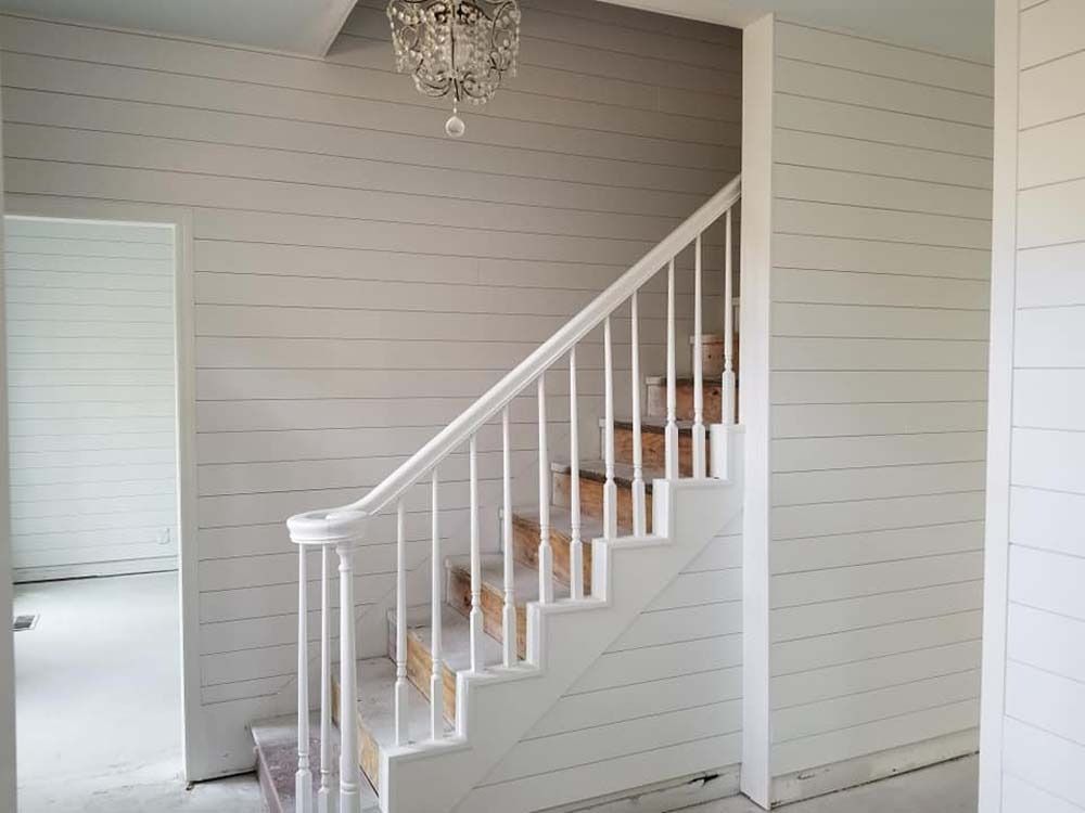 White staircase with wooden steps in a bright room with gray paneled walls and a chandelier