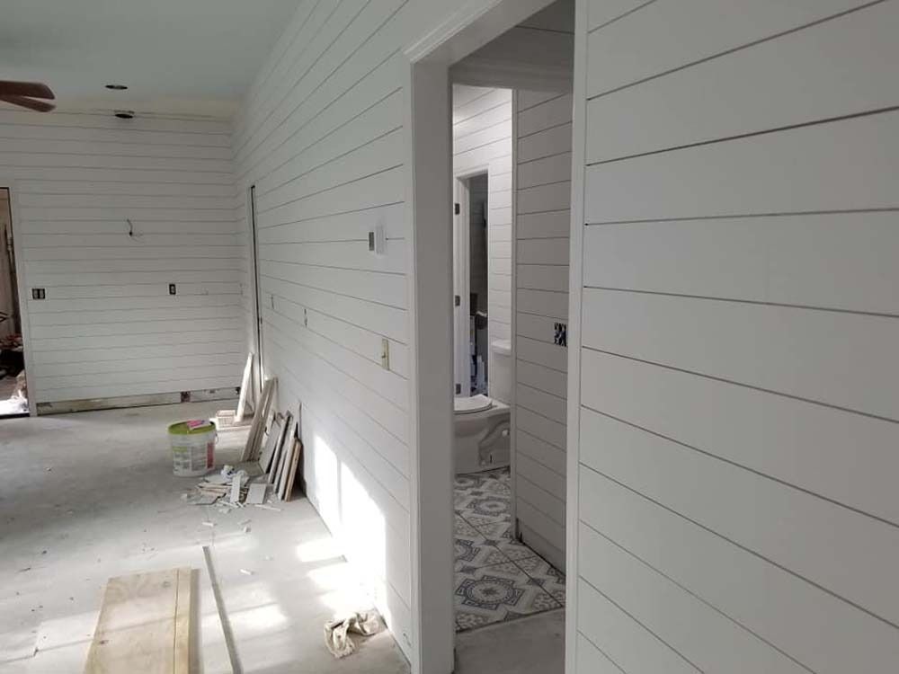 Bright white hallway with shiplap walls, open doorway, and construction materials on the floor