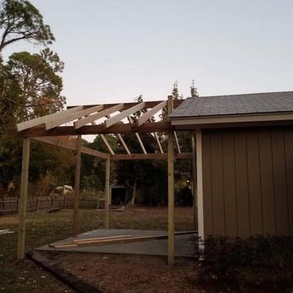 Partially built wooden pergola attached to a brown shed in a backyard at dusk