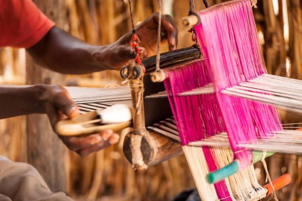 Person weaving bright pink and white threads on a loom, outdoors.