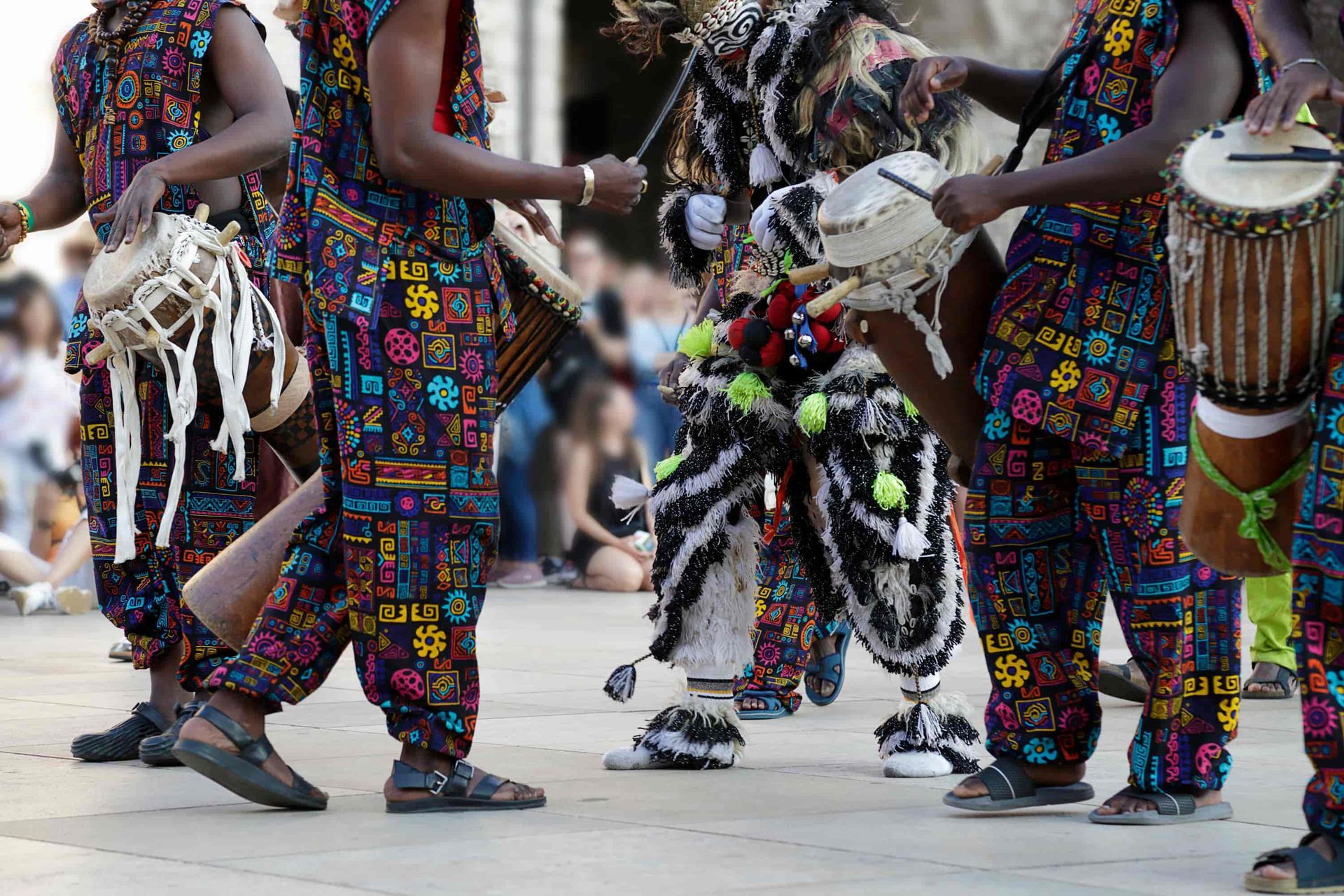 People in colorful patterned outfits playing drums outdoors.