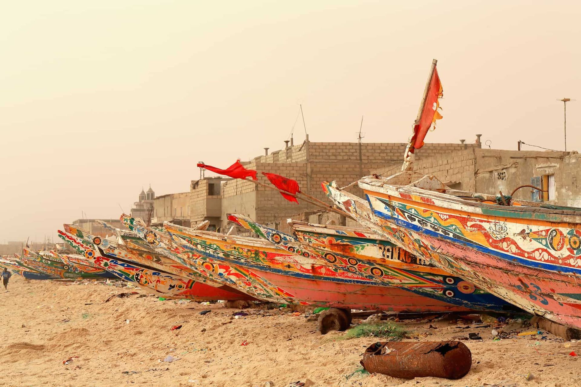 Colorful fishing boats lined up on a sandy beach, with buildings in the background.