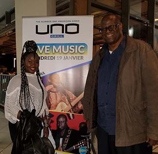 Two people pose in front of a promotional sign for live music at Uno Grill.