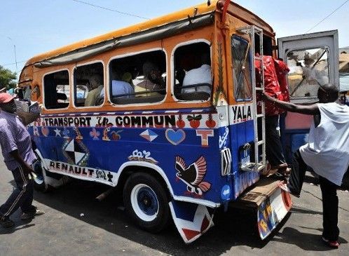 Colorful, crowded bus on a street. Passengers board, others wait.