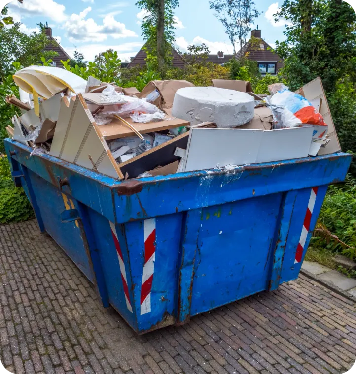 Blue dumpster overflowing with construction debris, outside, on a brick path.