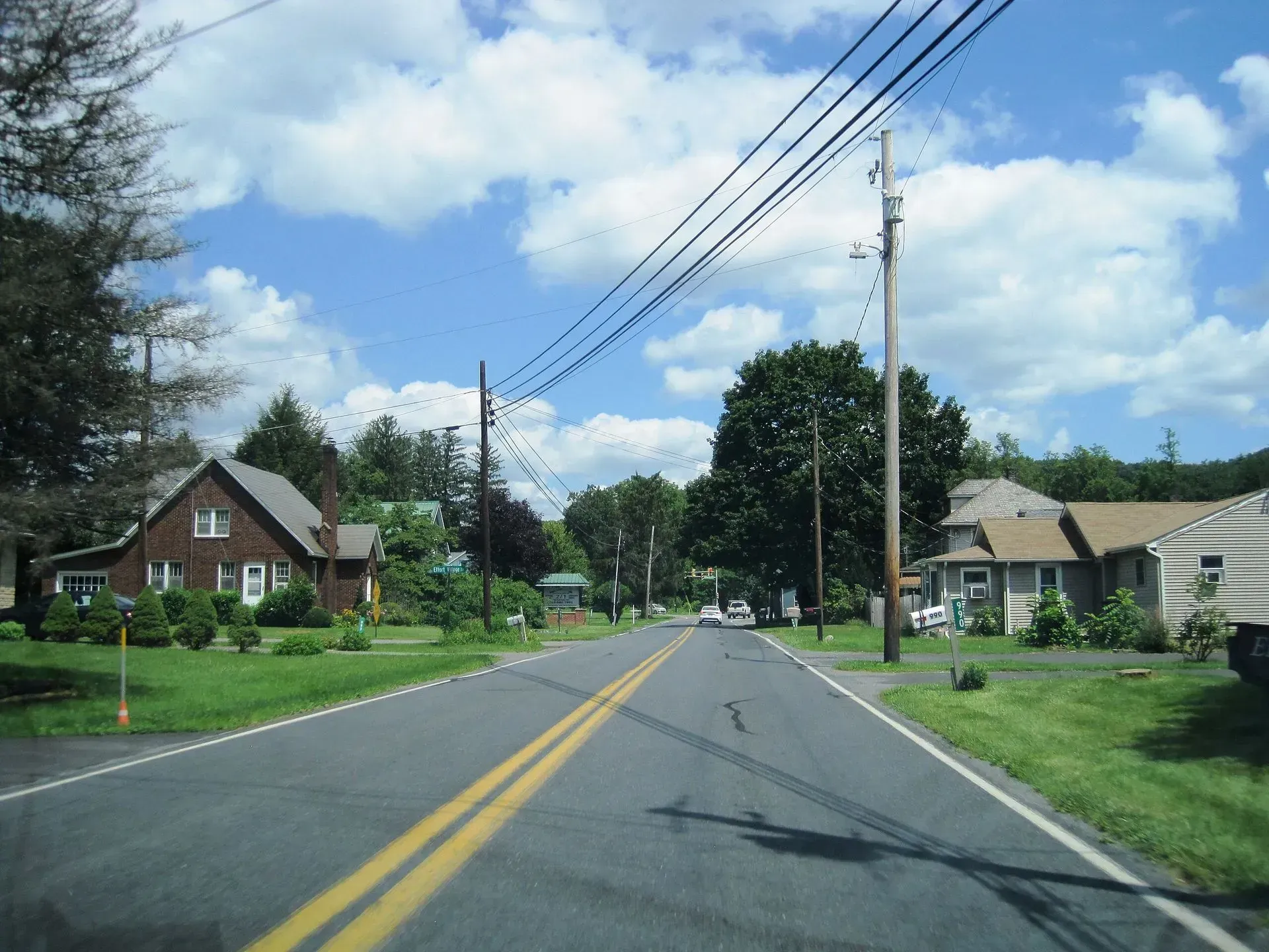 Residential street with houses, utility poles, and a partly cloudy sky