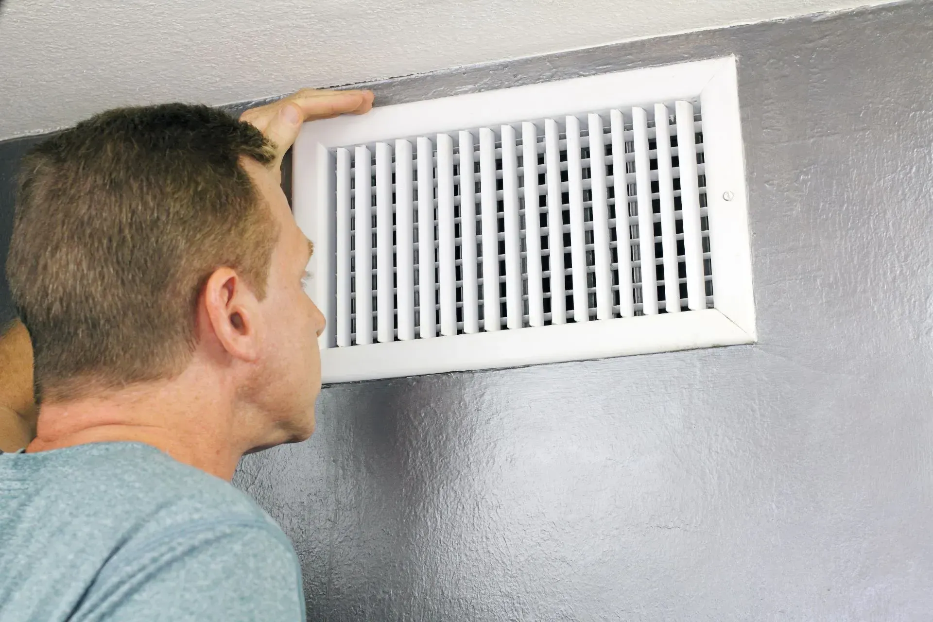 A man is looking at a vent on the wall.