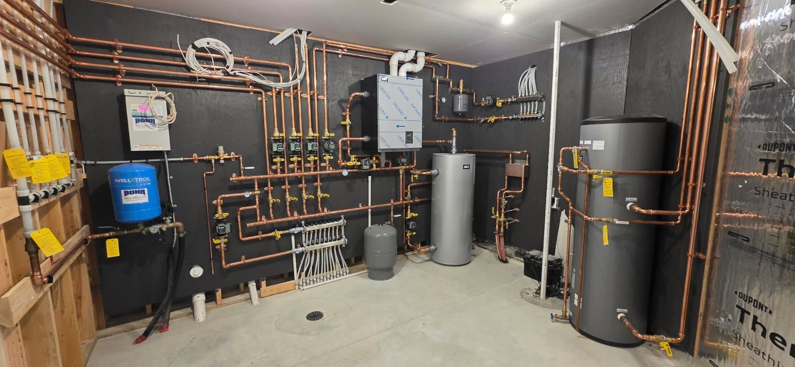 A room with copper pipes, tanks, and electrical components. The walls are black.
