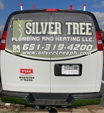 A silver tree plumbing and heating llc van is parked in a parking lot.