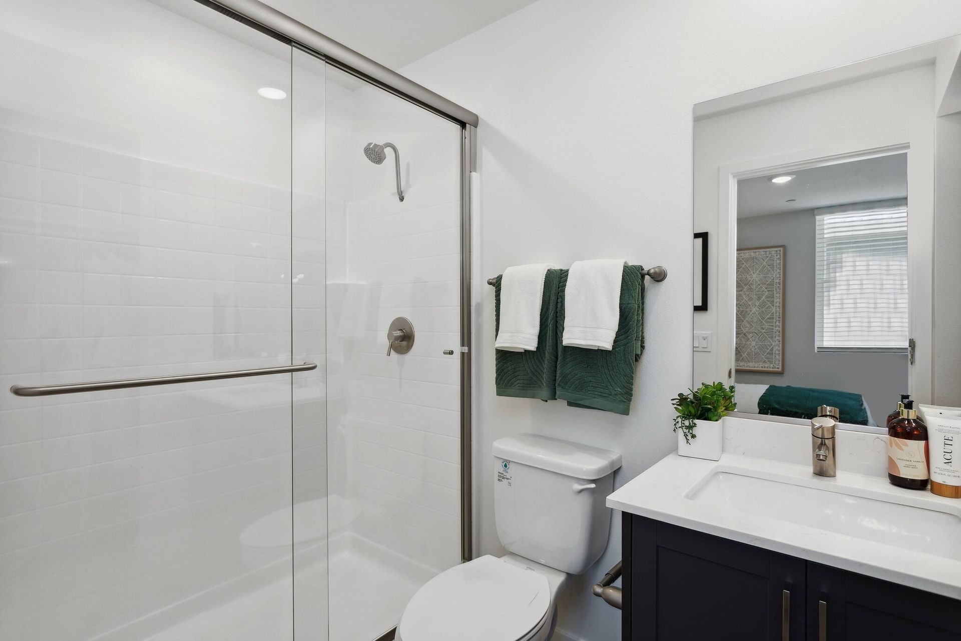 Sacramento apartment bathroom glass shower door, toilet, sink, and mirror at Maven on Broadway.