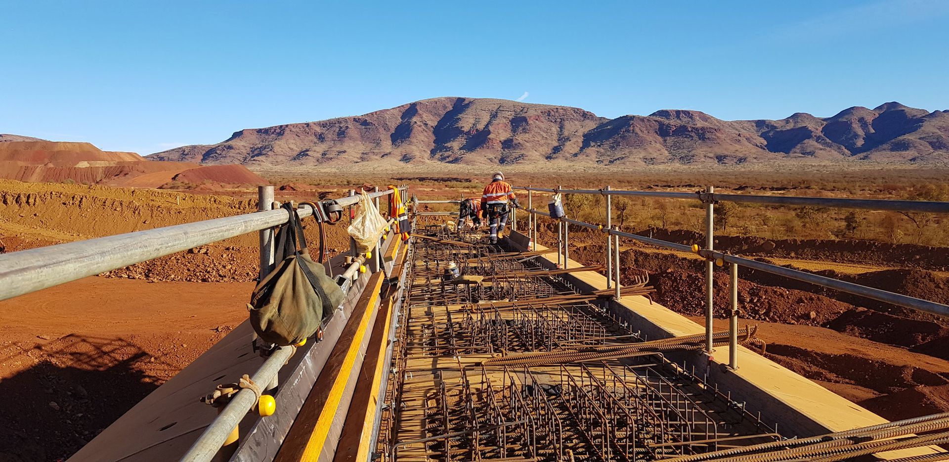 A bridge is being built in the middle of a desert with mountains in the background.