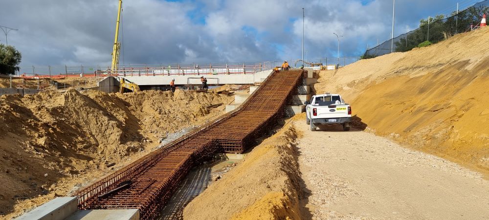 A white truck is driving down a dirt road next to a bridge under construction.