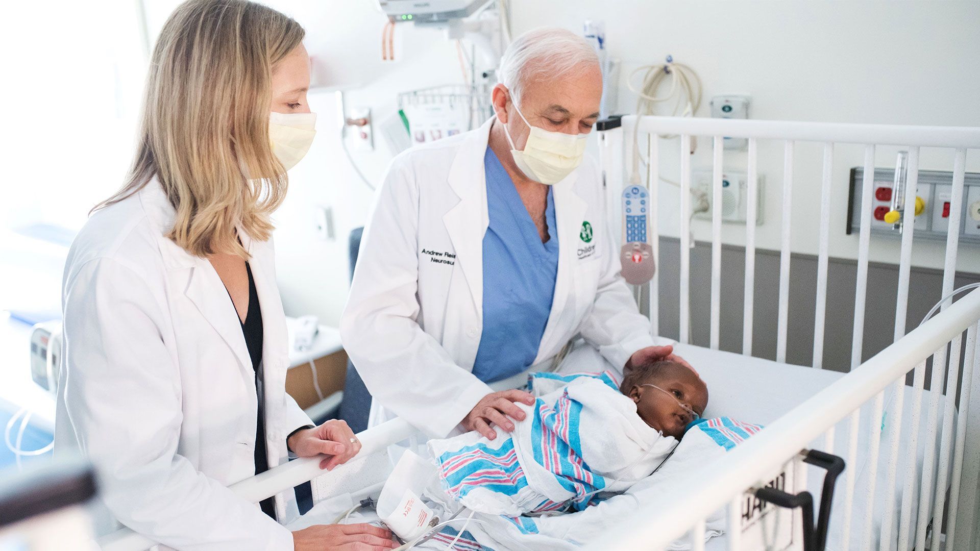 Doctors examining a newborn in a hospital crib, with a caregiver standing nearby