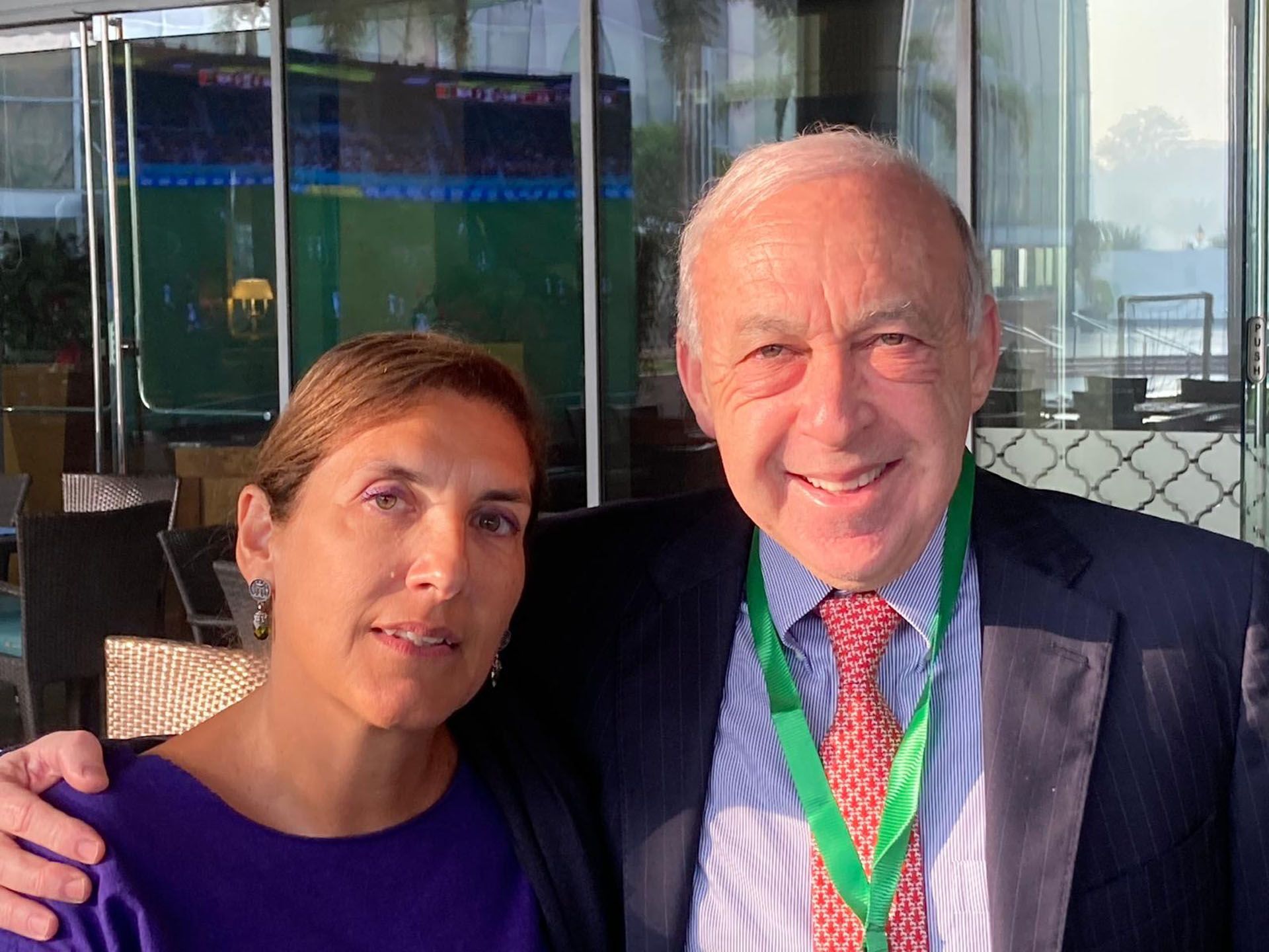 A woman and a man smiling at the camera outdoors. The man has a green lanyard.