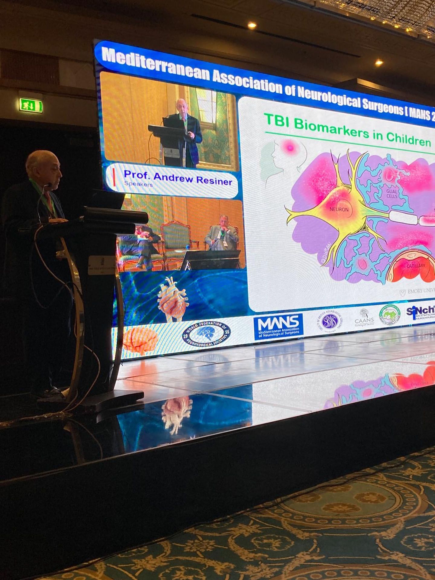 A speaker presents at a conference with a slide on TBI biomarkers in children.