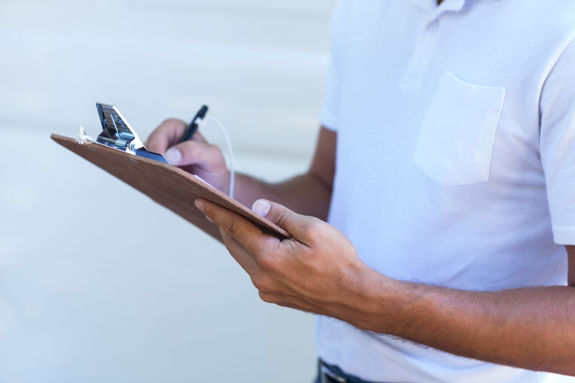 Person in white polo shirt writing on a clipboard.
