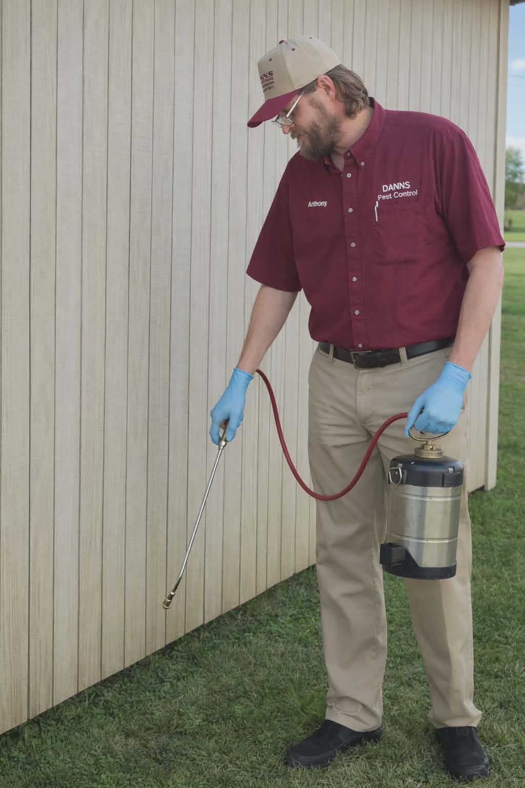 Pest control technician spraying a building's exterior with a metal tank sprayer.