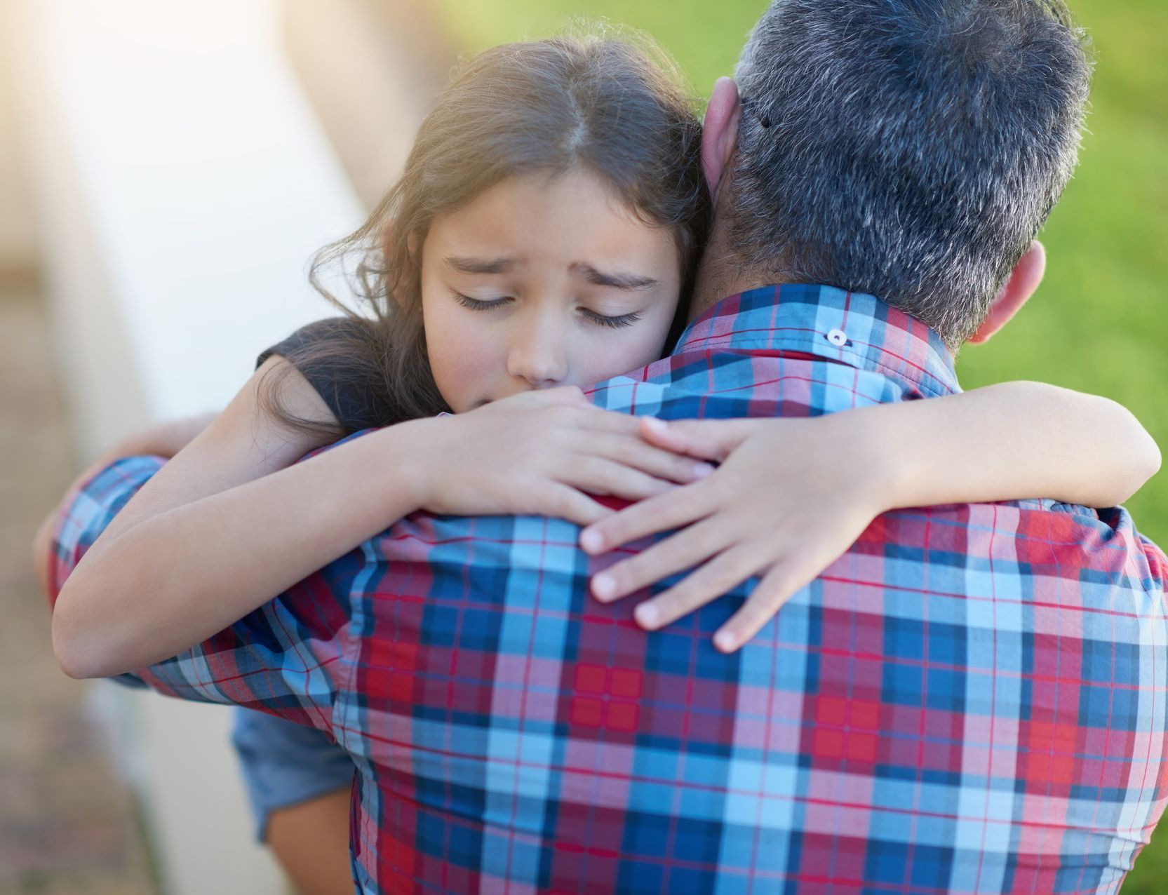 A little girl is hugging her father in a plaid shirt.