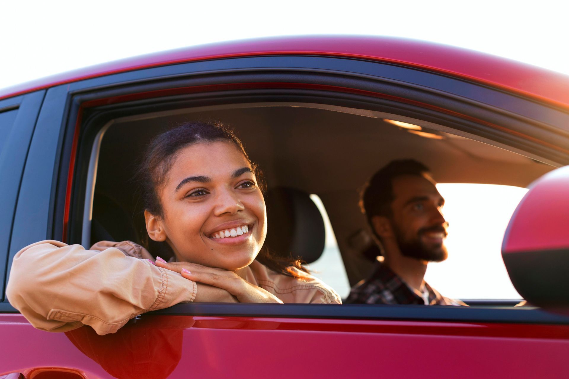 A man and a woman are sitting in a red car and smiling.