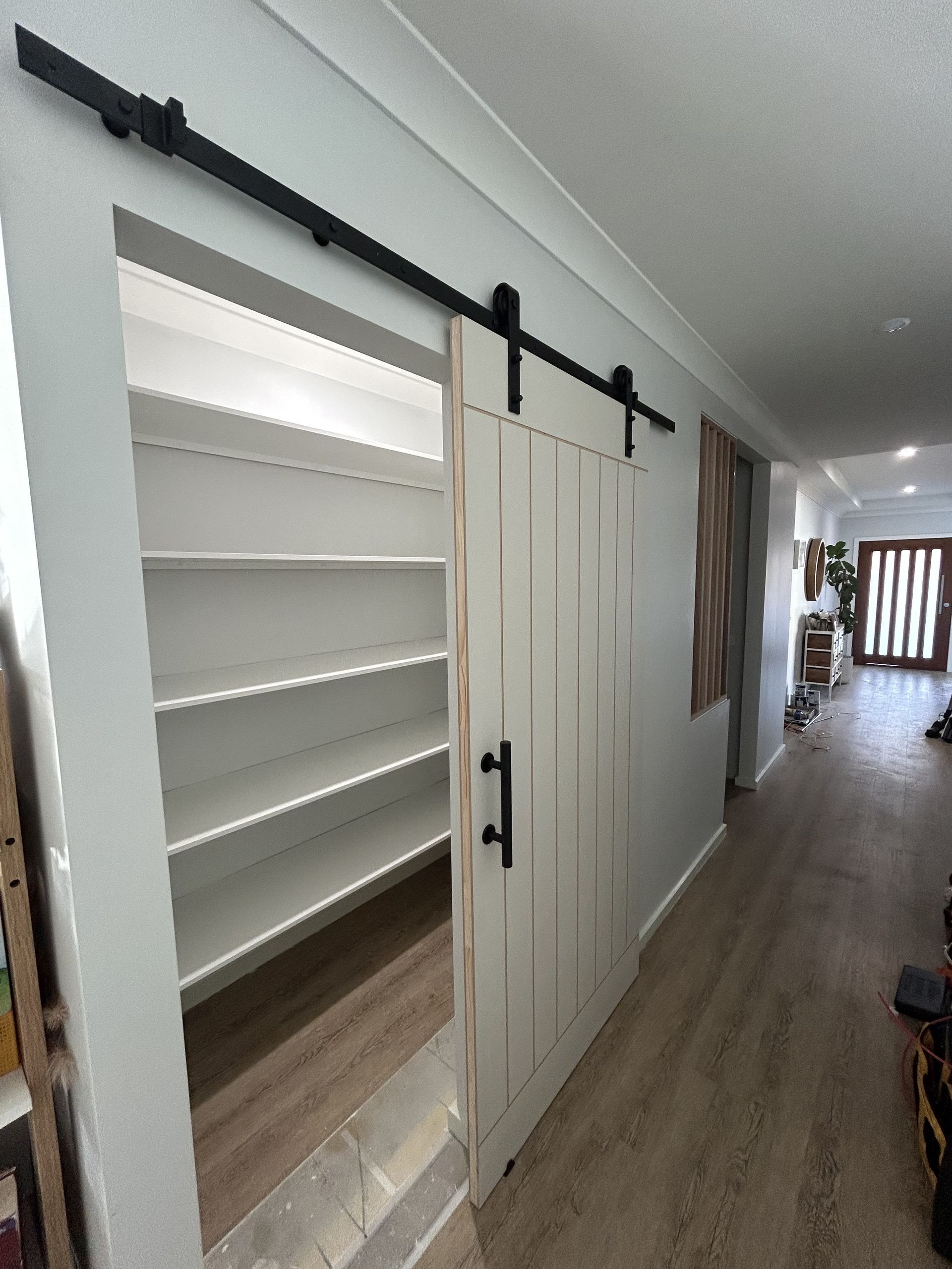 White pantry with sliding barn door, black hardware, and shelving. Interior hallway view — The Wright Way Building In North Albury, NSW