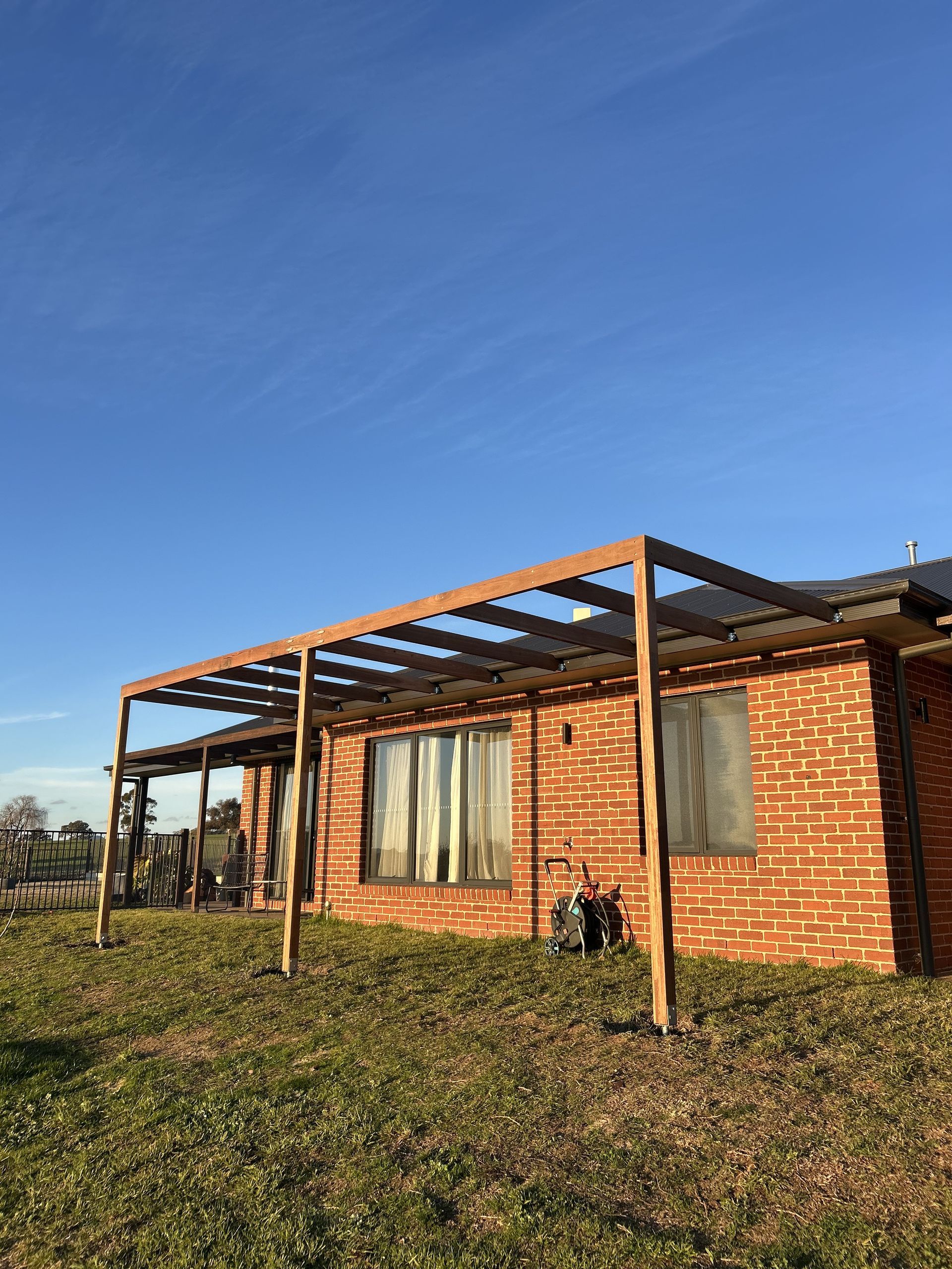 Pergola attached to a brick building, casting shadows on the grass under a blue sky — The Wright Way Building In North Albury, NSW