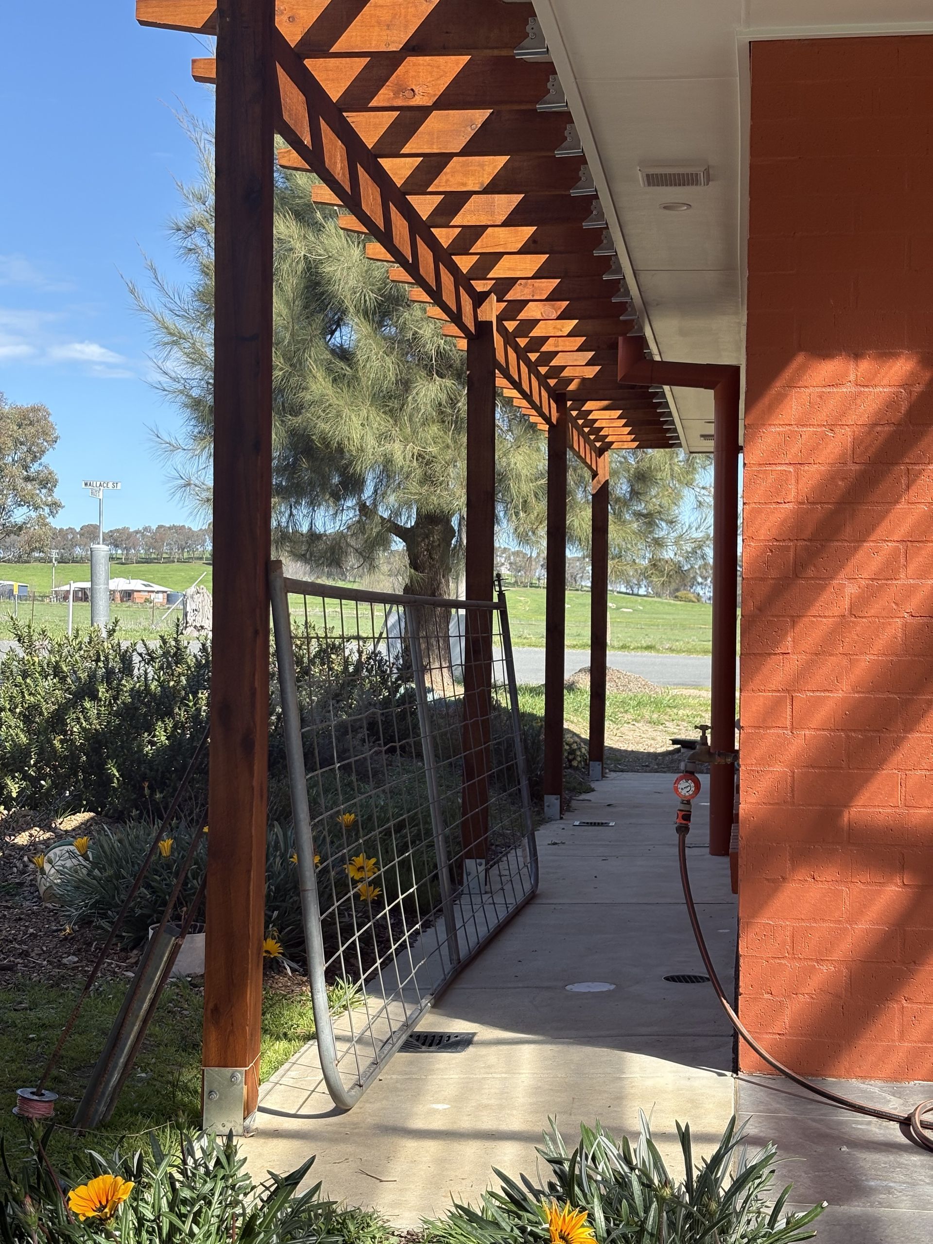 Covered walkway with a wooden trellis, beside a red brick wall and park — The Wright Way Building In North Albury, NSW