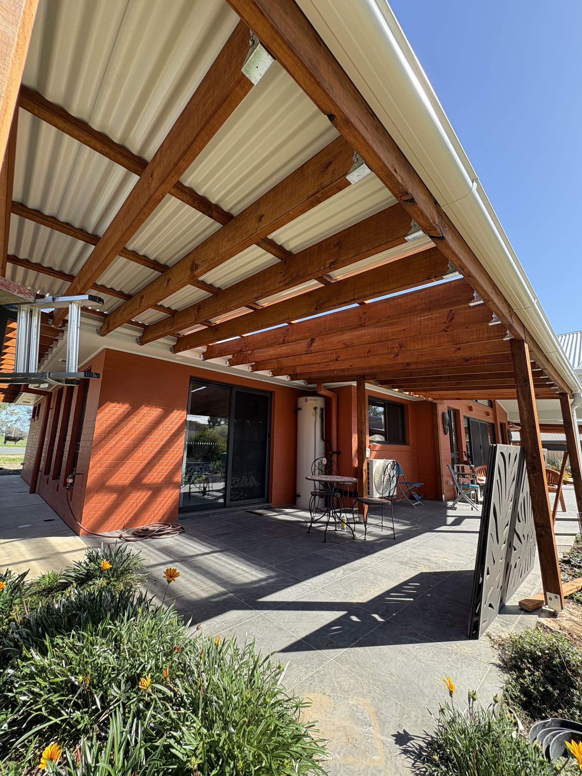 Orange building with wooden pergola roof, patio furniture, and plants outside on a sunny day — The Wright Way Building In North Albury, NSW