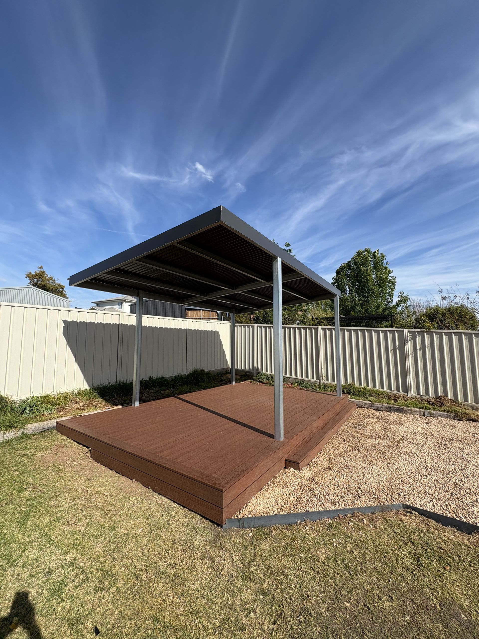 Wooden deck and pergola in a backyard, surrounded by grass and gravel, with a white fence and a blue sky — The Wright Way Building In North Albury, NSW