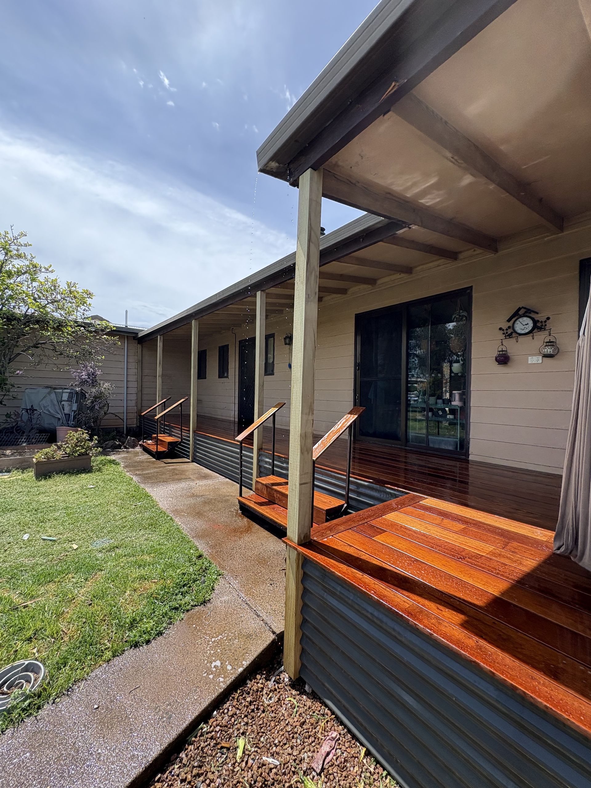 Exterior view of a house with a wooden deck and walkway. Green grass and blue sky are also visible — The Wright Way Building In North Albury, NSW
