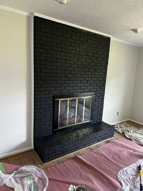Living room with black brick fireplace, brass firebox, and drop cloths on the floor during renovation