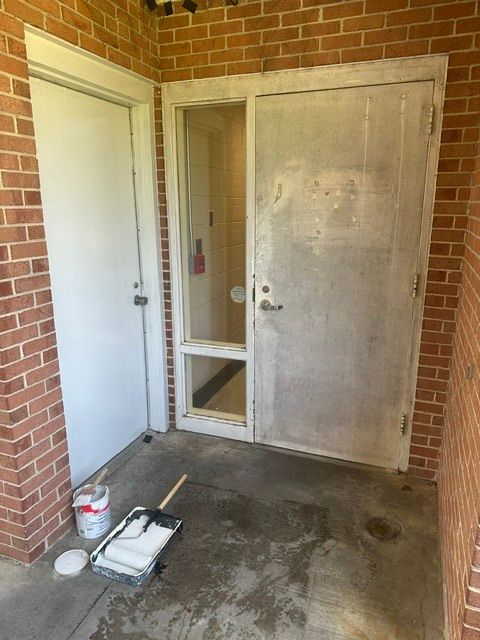 Front porch with white door, weathered screen door, brick walls, and paint supplies on the concrete floor