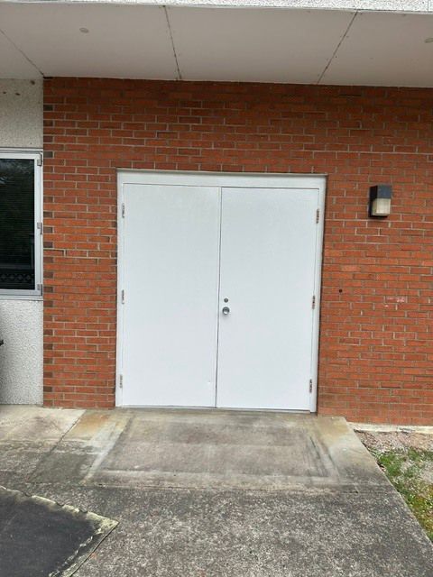 White double doors in a red brick wall with a small light fixture beside them.