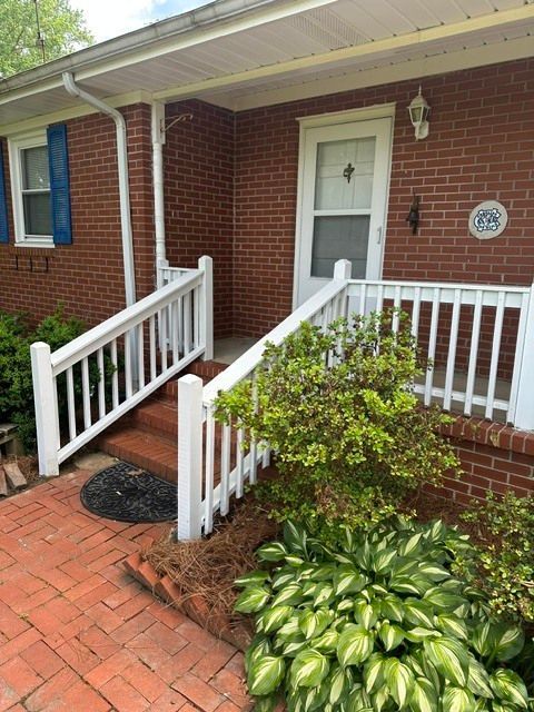 Brick house front porch with white railing, red brick steps, blue shutters, and green shrubs