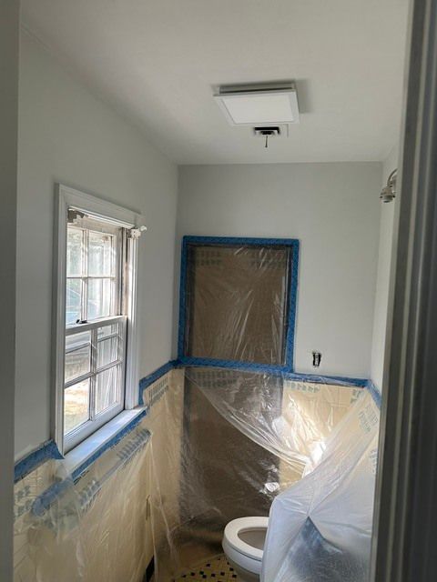 Bathroom under renovation, with plastic sheeting, blue painter’s tape, and a toilet visible.