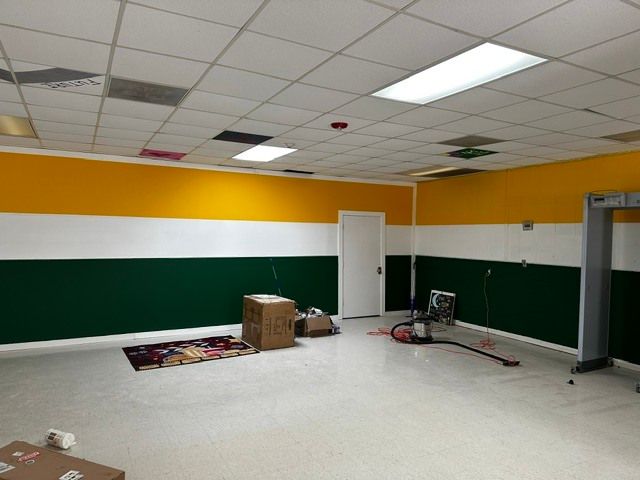 Empty room with yellow and green walls, ceiling tiles, and renovation materials on the floor